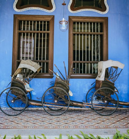 Two vintage rickshaws rest against a vibrant blue wall in George Town, Malaysia.